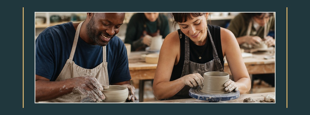 Two people shaping clay on pottery wheels in a workshop setting.
